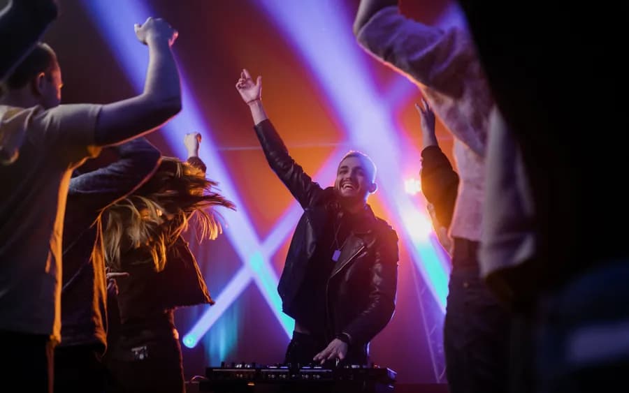 A DJ with hands raised over the decks as the floor dances