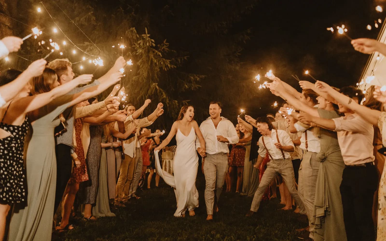 Wedding guests holding sparklers as the couple walk out between them